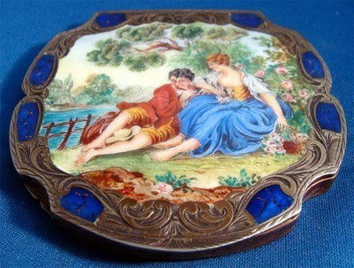 Italian Enamel .800 Silver Compact Man Playing Flute: Charming enamel painting of a couple by a stream, the man is playing a flute. The painting is framed by engraved silver and carnelian blue accents. Stamped "800 falacci firenzi" dimensions 3"x3" weigh