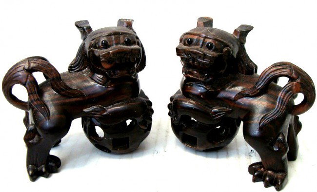 Pair Carved Wood Chinese Fu Dogs: Each dog has a ball in its mouth that rolls around when yoiu move it, and they stand on a chinese puzzle ball that moves. Carved from a dark wood. Dimensions each 4" long by 4" tall.