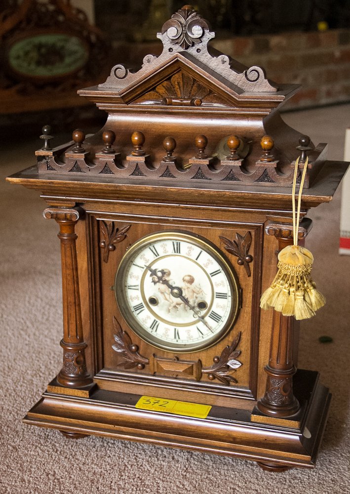 German Mantle Clock: (1) 20" h. Walnut architectural case. White porcelain face with hand painted scene of two cherubs. Eight day spring wound movement with time and strike on the hour and half hour. Shipping: USPS or Fed
