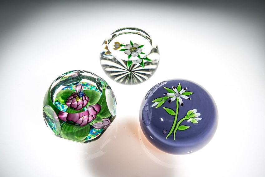 (3) Perthshire Paperweights: (3) Total Perthshire Paperweights. Including: 3 1/2" flower on a purple base. (1) 2 3/4" Floating white flower. (1) 1983 pink flower on a polychrome background. All have the P cane mark.