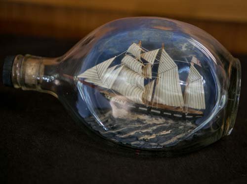 Haig's Ship in a Bottle: (1) 8"w. Ship in a bottle on blue painted waves. Marked on base. Ship name: Jenny.
