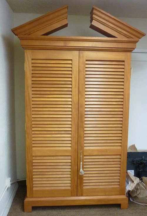 Donghia Armoire: (1) 58"w (48"w without top) x 24"d x 98"h (78"h without top piece) Donghia by John Hutton. Teak with a natural finish.Crested with a protruding cornice. One pair of bifolding doors with a wood slat fr