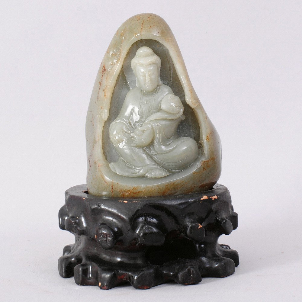 A FINE CHINESE CARVED HETIAN JADE GUANYIN ON STAN: CARVED HETIAN JADE WITH RUSSET SKIN TO DEPICT A SEATED GUANYING HOLDING A RUYI, COMES WITH WOOD STAND.