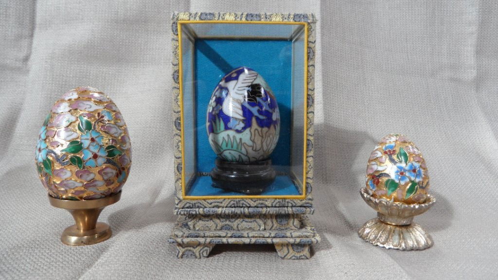 CHINESE CLOISONNE EGGS: CHINESE,ASSEMBLED GROUP OF THREE CLOISONNE EGGS IN THREE DIFFERENT SIZES,TWO ARE HAVING LAND SCAPE OF NICE FLOWERS AND LEAVES ON GOLD BACKGROUND AND SITTING ON THE STAND,THE MIDDLE EGG IS HAVIND NICE