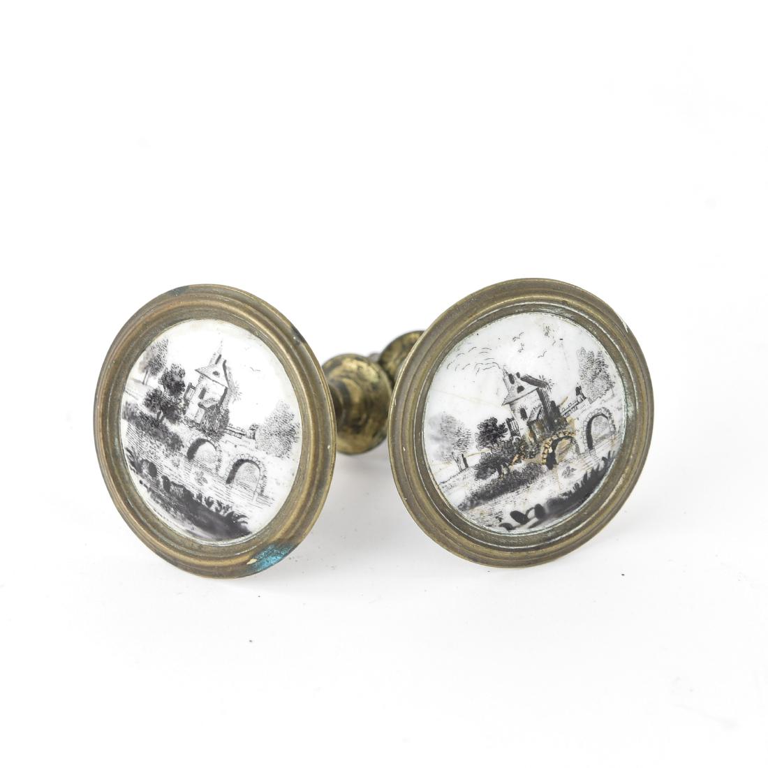 (2) PAINTED PORCELAIN AND BRASS TIE BACK KNOBS: In a wooden box. Dimensions: (Each knob) H 3" x Dia. 2" Condition: Cracks and repair to face of one. Some tarnish and patina to brass.