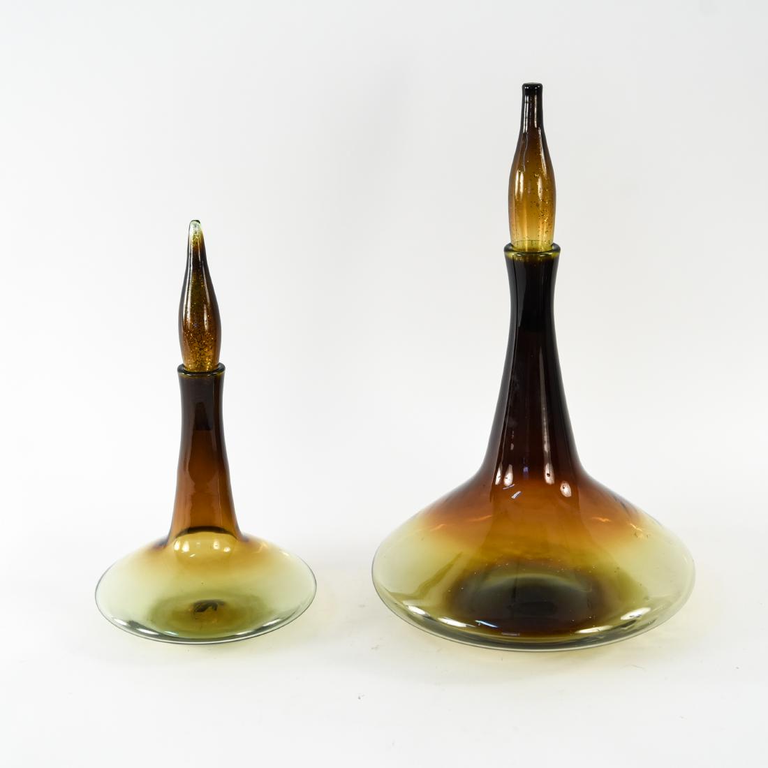 (2) GREENWICH FLINT CRAFT ATOMIC GLASS DECANTERS: By Thomas Connally in burnt honey. American, 1960's. Dimensions: (Larger) H 19.75" x Dia. 11.75" Condition: Small loss to stopper portion of finial on smaller decanter.
