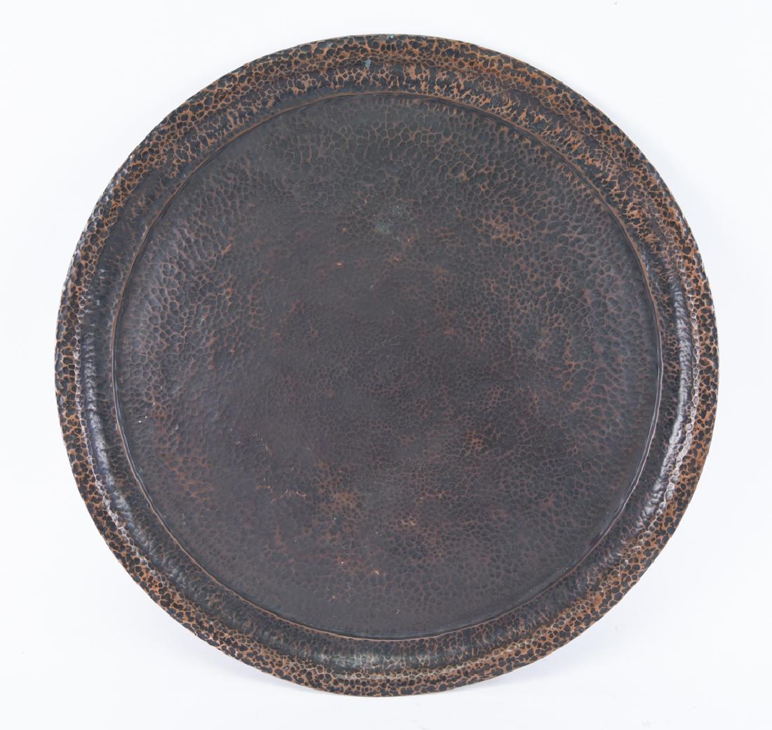 ARTS AND CRAFTS HAMMERED COPPER TRAY: Joseph Heinrichs, marked underneath. Arts and crafts style with darkened surface. Dimensions: H 1" x Dia. 22.5" Condition: Some unevenness to surface coloration.