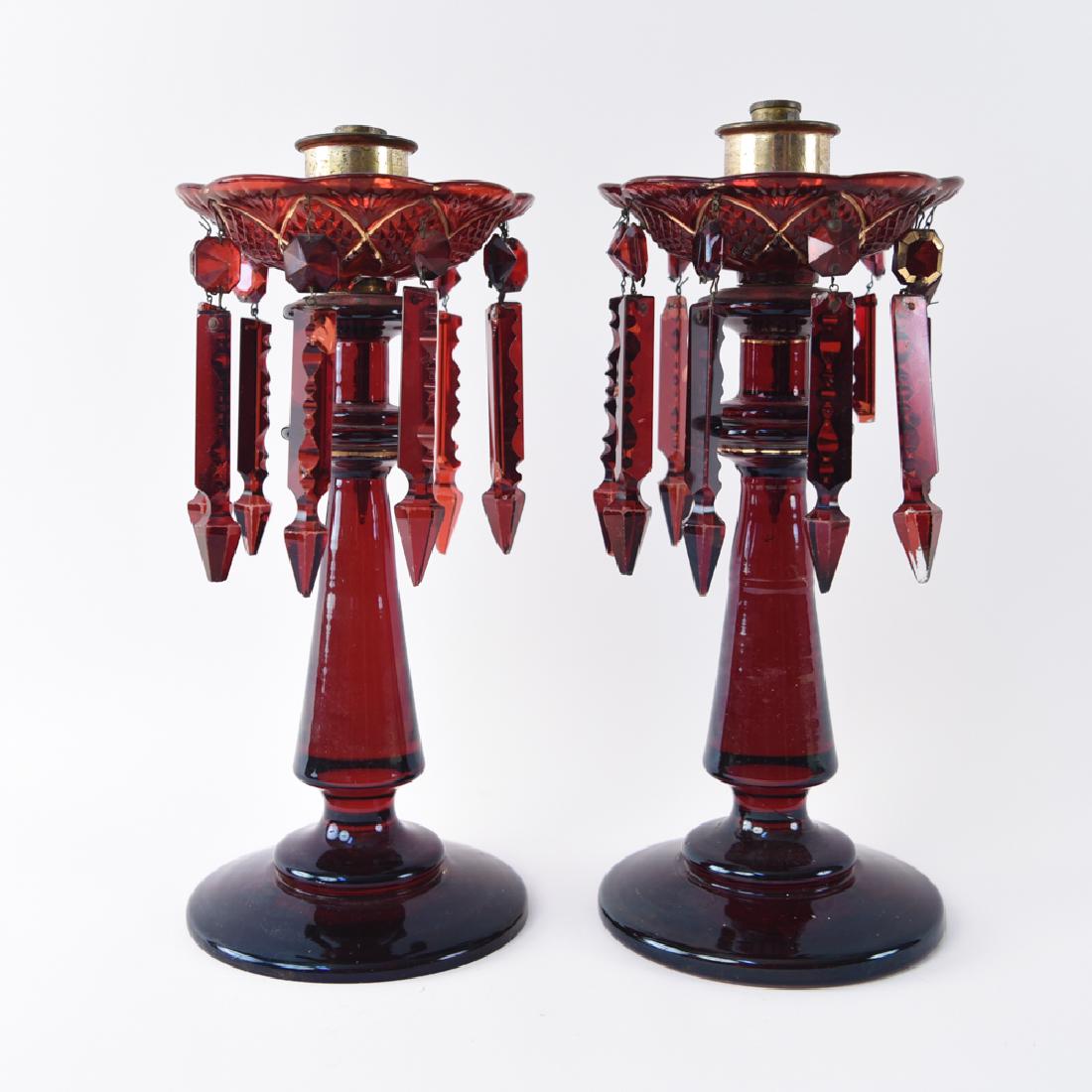 CRANBERRY GLASS CANDLESTICK MANTLE LUSTERS: Dimensions: H 14" x Dia. 5.5" Condition: Some tarnish to fittings. Wear to gilded decoration. Few chips throughout.