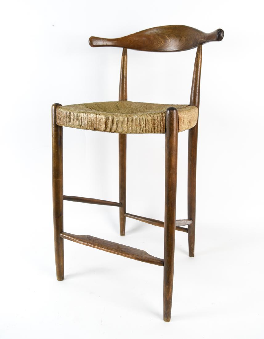 MANNER OF HANS WEGNER ELBOW BAR STOOL: Dimensions: H 34.5" x W 19" x D 17.5" x SH 23.75" Condition: Repair to backrest. Surface wear and fraying to few areas of rush seat. Scuffs and wear to wood. Break to wood where backrest meets post. F
