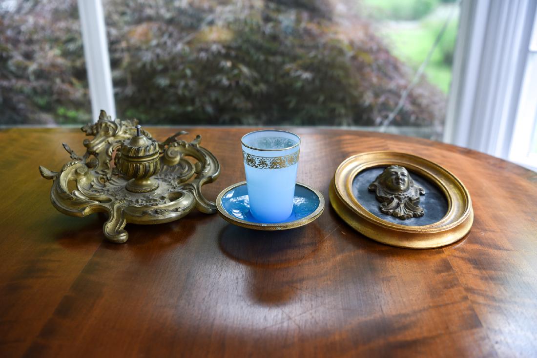 19TH C. ORMOLU ARTICLES: Including inkwell, decorative mask, and cup with bronze rimmed saucer. Dimensions: (Inkwell) H 4" x W 9" x D 9.75" Condition: Missing glass insert for inkwell. Mask loose in frame. Areas of patina.