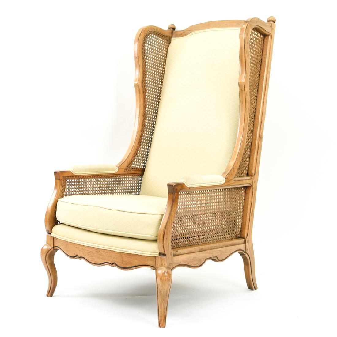 CANE AND UPHOLSTERED WINGBACK CHAIR: Dimensions: H 48" x W 25" x D 28" x SH 17" Condition: Showing very light wear overall. Few rubs and signs of use. Area of finish wear to back leg.