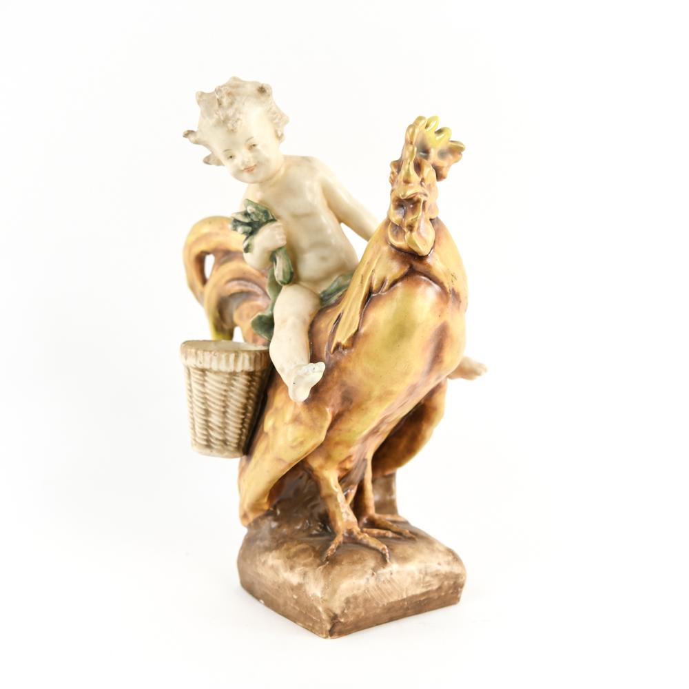 AMPHORA PORCELAIN FIGURE RIDING ROOSTER: Marked with Amphora, R, and numbers underneath. Dimensions: H 13.5" x W 9.75" x D 7" Condition: Repair to boy's neck. Crazing. Some surface rubbing and wear. Few minor chips.
