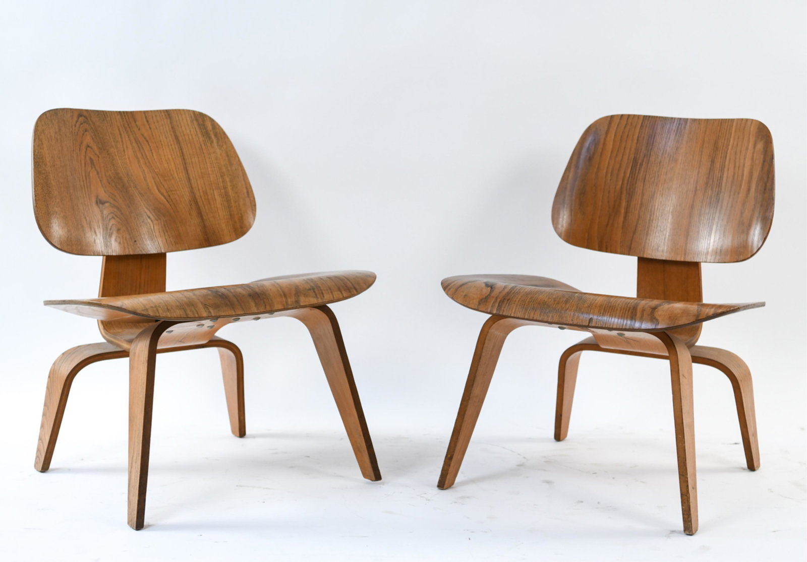 (2) CHARLES & RAY EAMES HERMAN MILLER LCW CHAIRS: Mid-Century, no labels. Dimensions: H 26.5" x W 21.75" x D 22" Condition: Some newer screws, sturdy, some roughness and surface scratching to seat surface, uneven finish signs of use and age