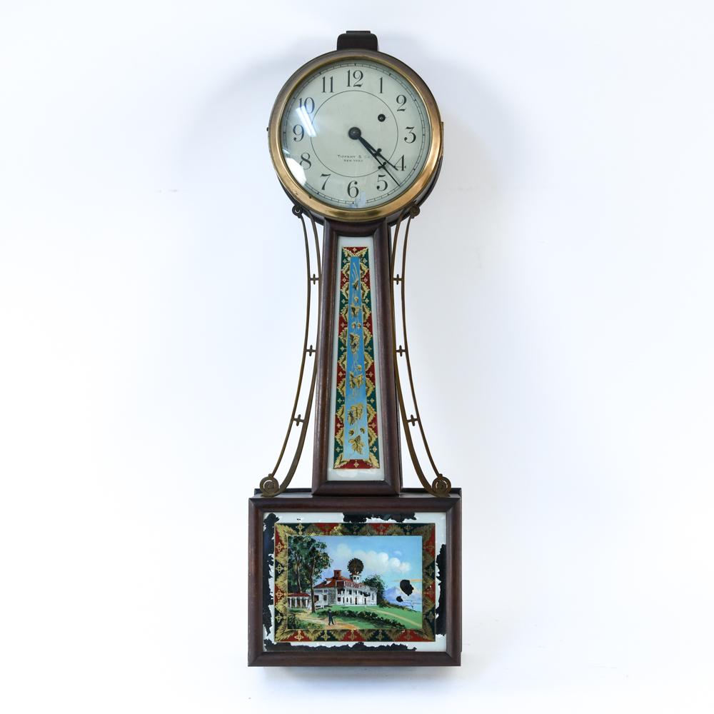 TIFFANY AND CO. NEW YORK WALL BANJO CLOCK: Mahogany eagle mounted banjo clock with eglomise stem and lower panel. Tiffany & Company. Dimensions: H 31" x W 11" x D 4" Condition: Losses to finish on face and edges. Not tested.