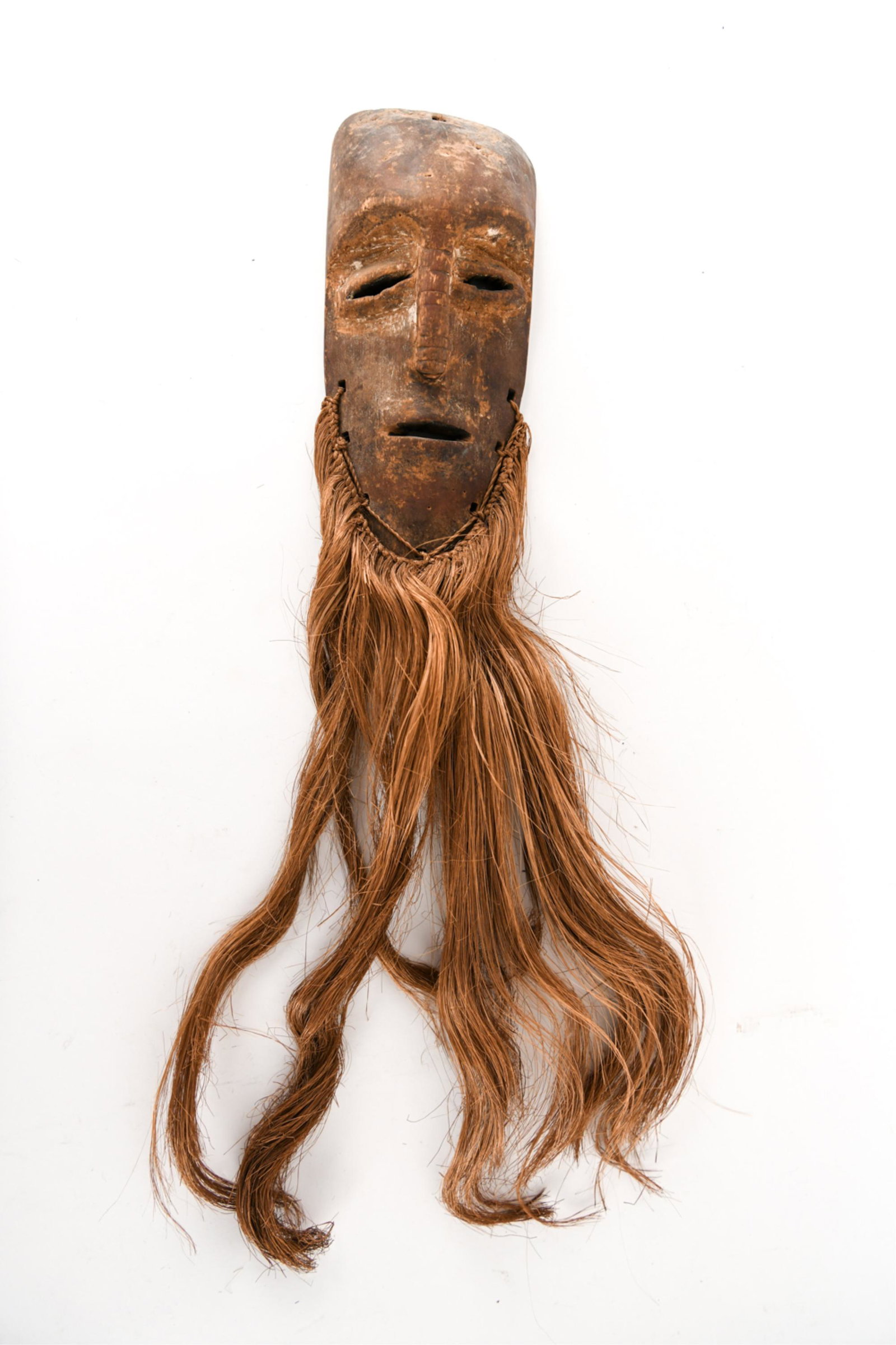 VINTAGE AFRICAN MASK: Thin mask. With remains of pigment. Vegetable fiber beard attached. Possibly pre-1940s. Dimensions: H 24" x W 4.5" Condition: Age wear. Some surface distress.