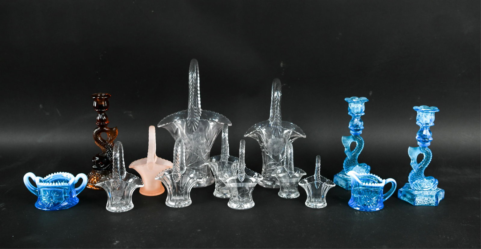 GROUPING OF DECORATIVE PRESSED GLASS: (14) pieces. Including baskets, dolphin candlesticks, creamer, sugar, etc. Dimensions: (Tallest basket) H 13" x W 7.75" x D 5" Condition: Minor surface wear.