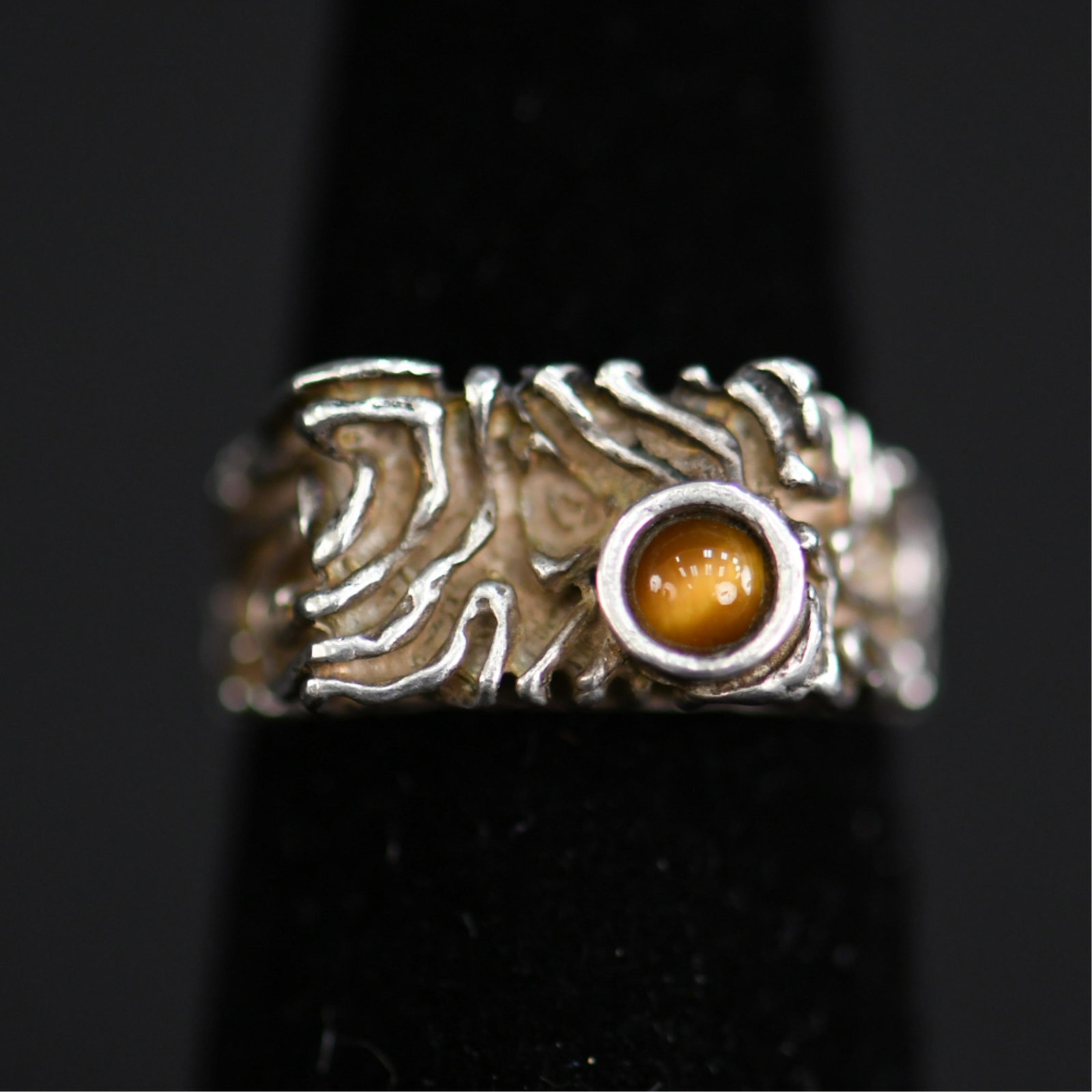 MID-CENTURY BRUTALIST TIGERS EYE & SILVER RING: No hallmarks. Sterling silver and tigers eye. Dimensions: Face: 0.75" Ring Size: 6 Condition: Showing light signs of use and age.