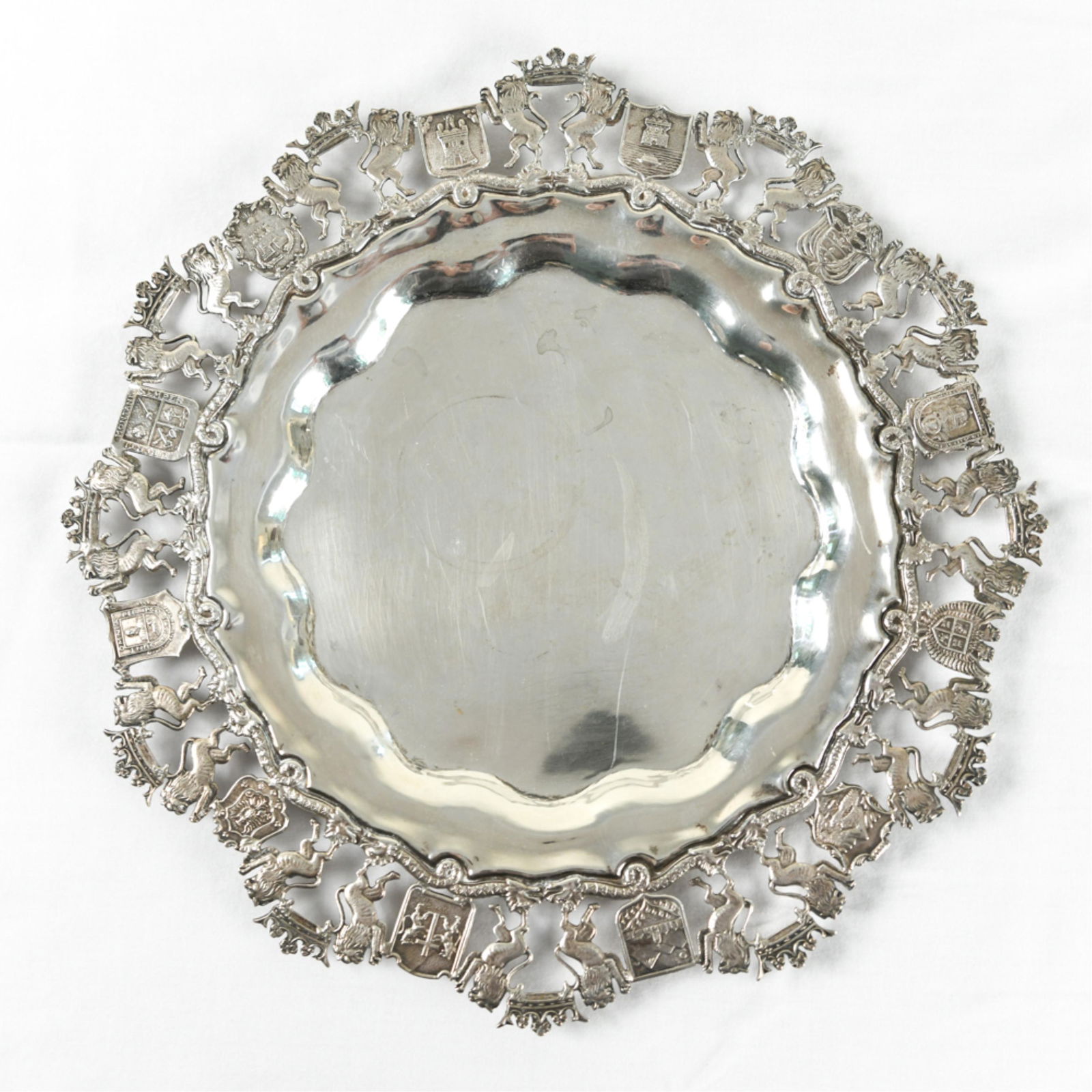 900 SILVER CHARGER PLATE: 900 silver. Lion, crown, and shield motif border.Dimensions: Dia. 12.75"Weight: 18.430 oztCondition: Signs of use including some slight bends to edge.