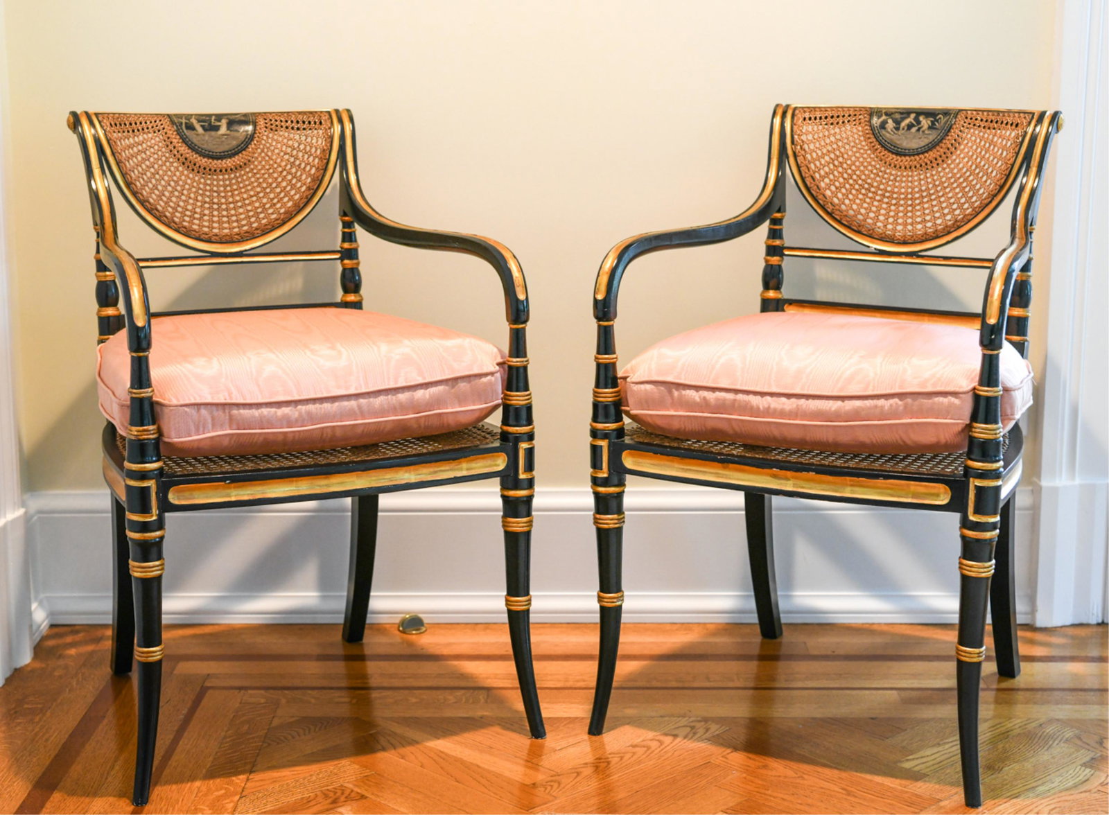 PAIR OF REGENCY STYLE EBONIZED ARMCHAIRS: With caning and paint decoration. Seats with down and foam filling. May be made by Smith and Watson Dimensions: H 33.25” x W 21.75” x D 24” x SH 21” Condition: Couple small chips to paint fini