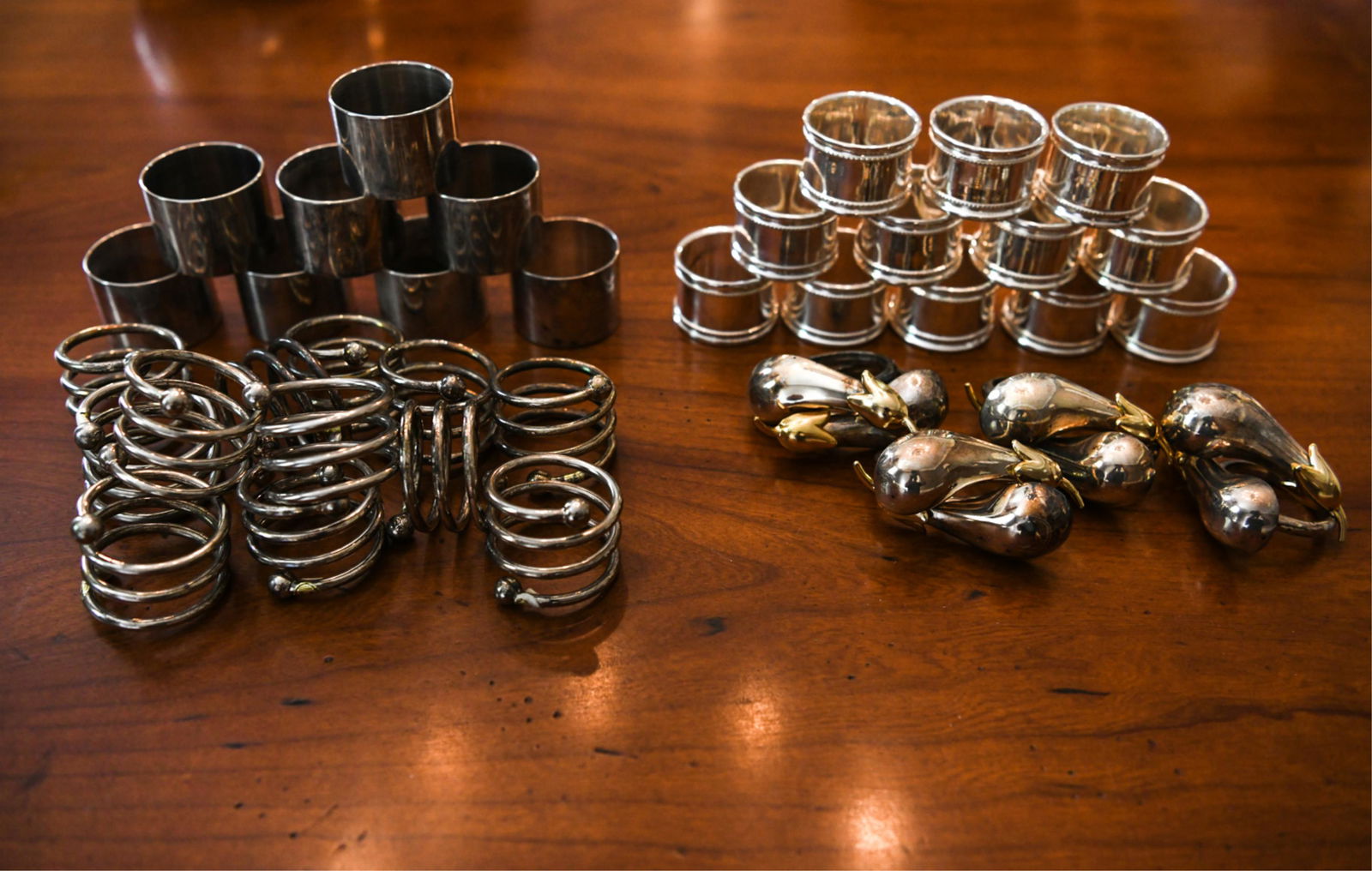 GROUPING OF NAPKIN RINGS: Including eggplant form, spring form, simple, etc. Dimensions: (Eggplant) H 3" x W 2" x D 1.25" Condition: Showing light signs of use including some tarnish.