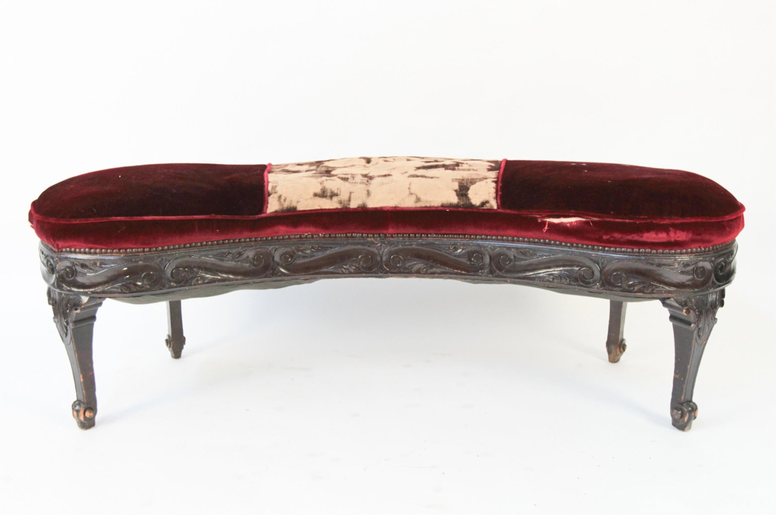 CARVED AND UPHOLSTERED BENCH: Carved wooden legs with upholstered seat. Dimensions: H 19" x W 61" x D 21" Condition: Upholstery has rips and losses throughout. Floral pattern fading. Wooden base with dents and scratches.