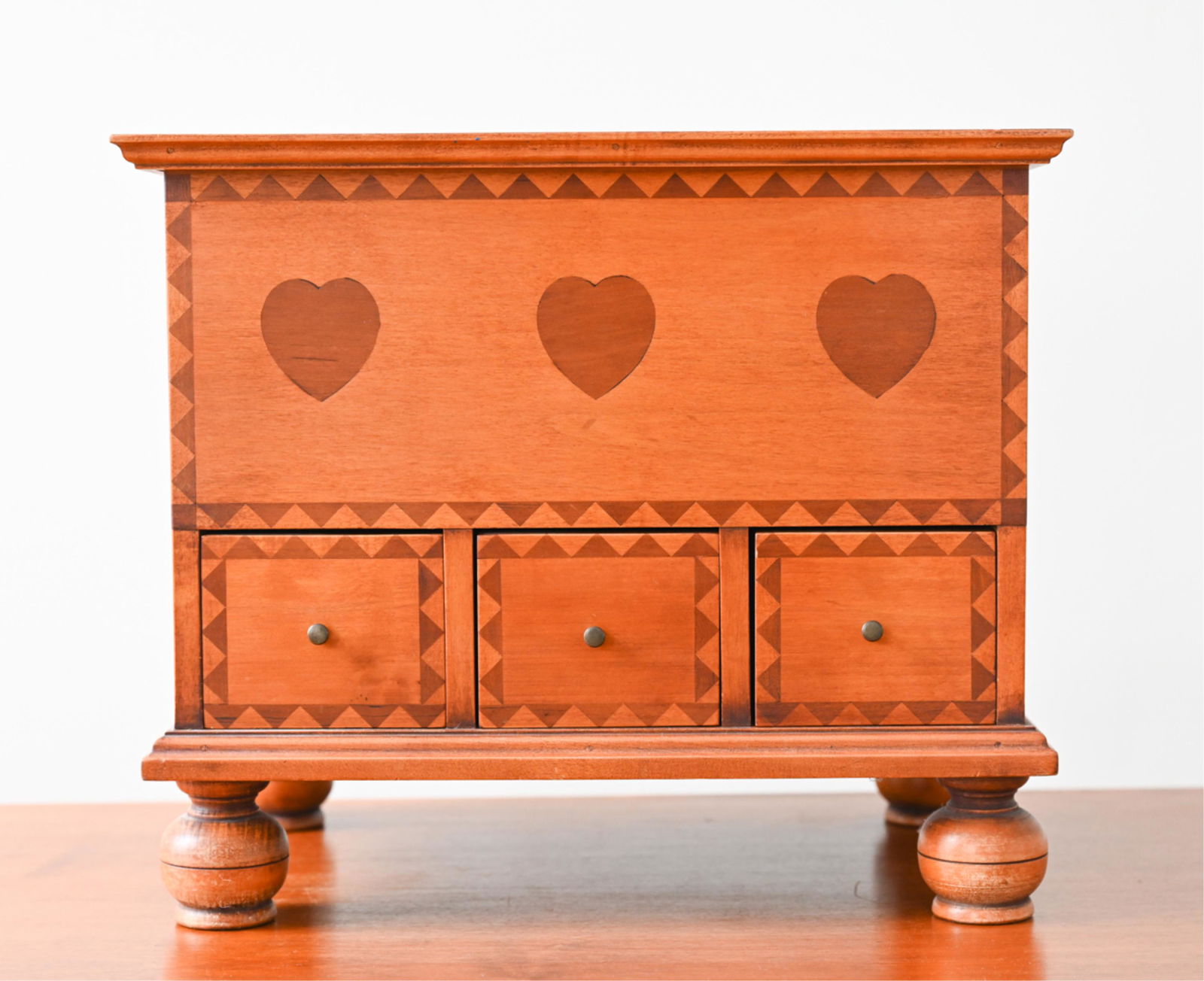 ELDRED WHEELER FOOTED KEEPSAKE JEWELRY CHEST: Lidded three-drawer chest, marked on bottom, with heart inlay and bun feet. Dimensions: H 13.75" x W 16.25" x D 11.25" Condition: A few nicks to edges, light wear consistent with age and use.