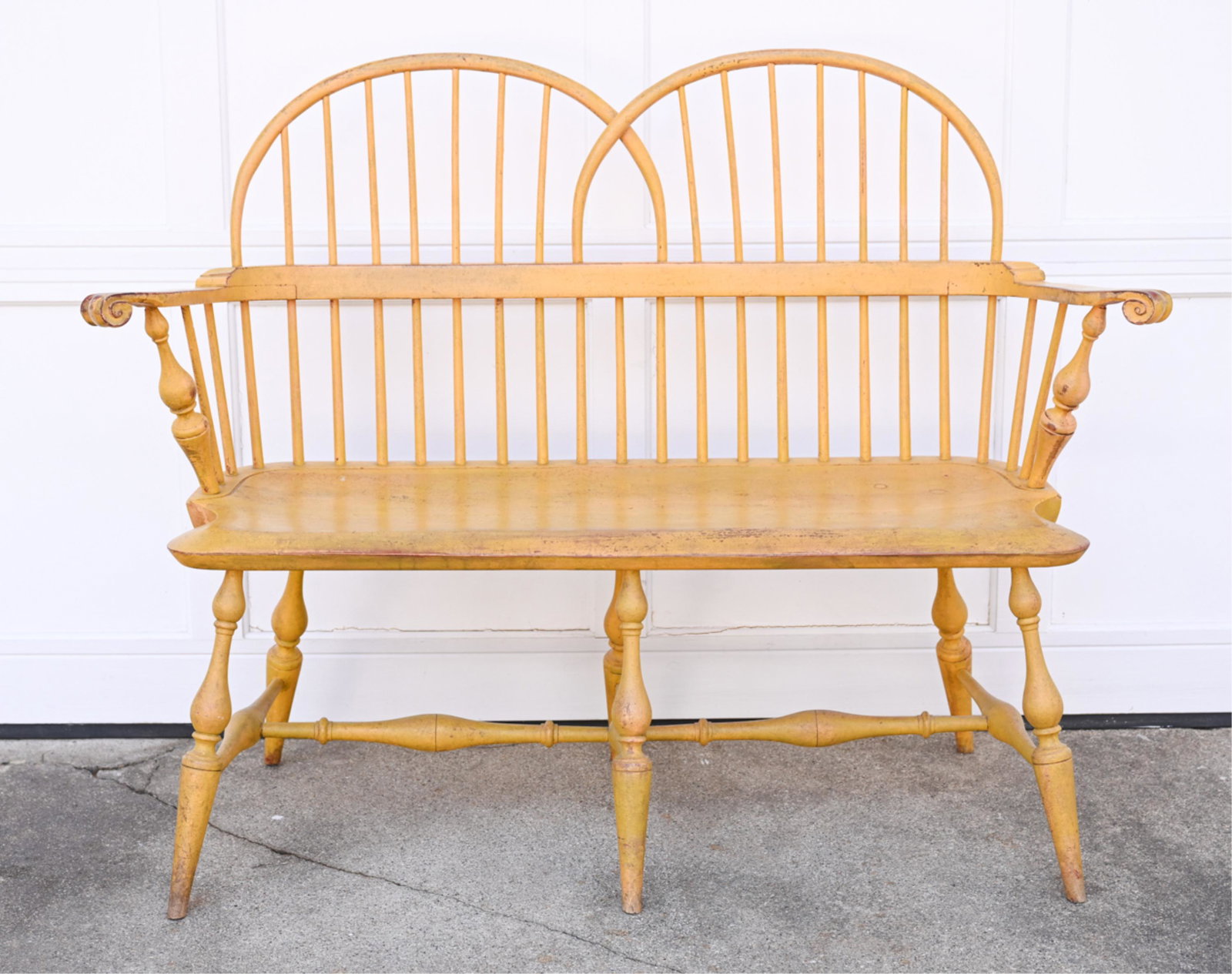 PAINTED SPINDLE-BACK WINDSOR STYLE BENCH: Apparently unlabeled, with turned spindles and scroll arms. Dimensions: H 37" x W 50" x D 17" x SH 17" Condition: Intentionally distressed, with some scratches, scuffs, and losses to paint.