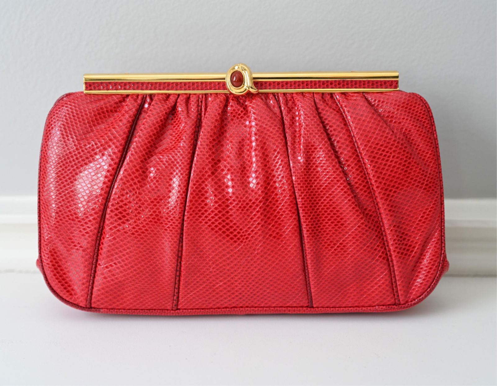 JUDITH LEIBER EXOTIC LIZARD LEATHER CLUTCH: Gold-tone hardware, with cabochon stone closure, herringbone chain shoulder strap, red satin lining and interior zip pocket. With original double-sided compact mirror and comb. Dimensions: H 5.5" x W