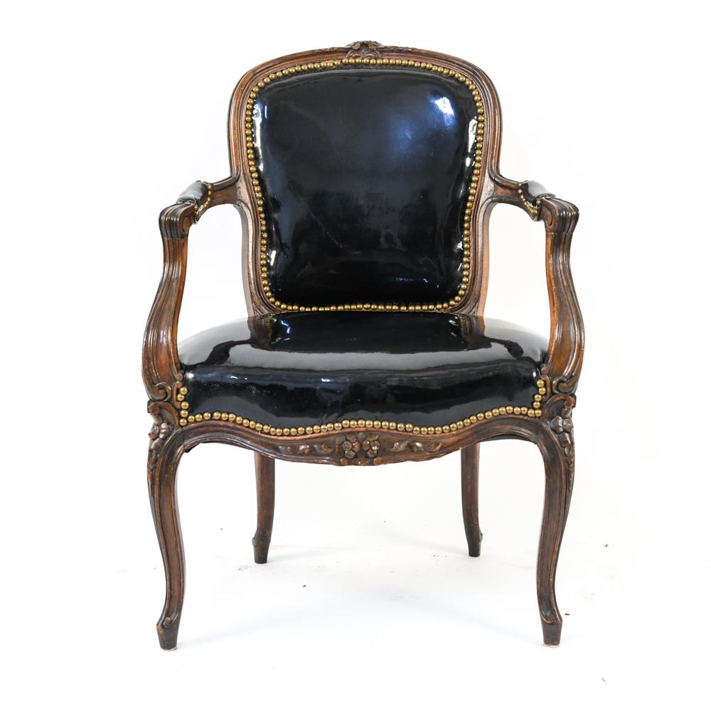 LOUIS XVI STYLE CARVED WIDE-SEAT FAUTEUIL ARMCHAIR: Carved floral back, scrolled arms, nail-head trim, and faux patent leather vinyl upholstery with extra-wide seat. Dimensions: H 34.5" x W 24.5" x D 19" x SH 16.75" Condition: Wear consistent with age 