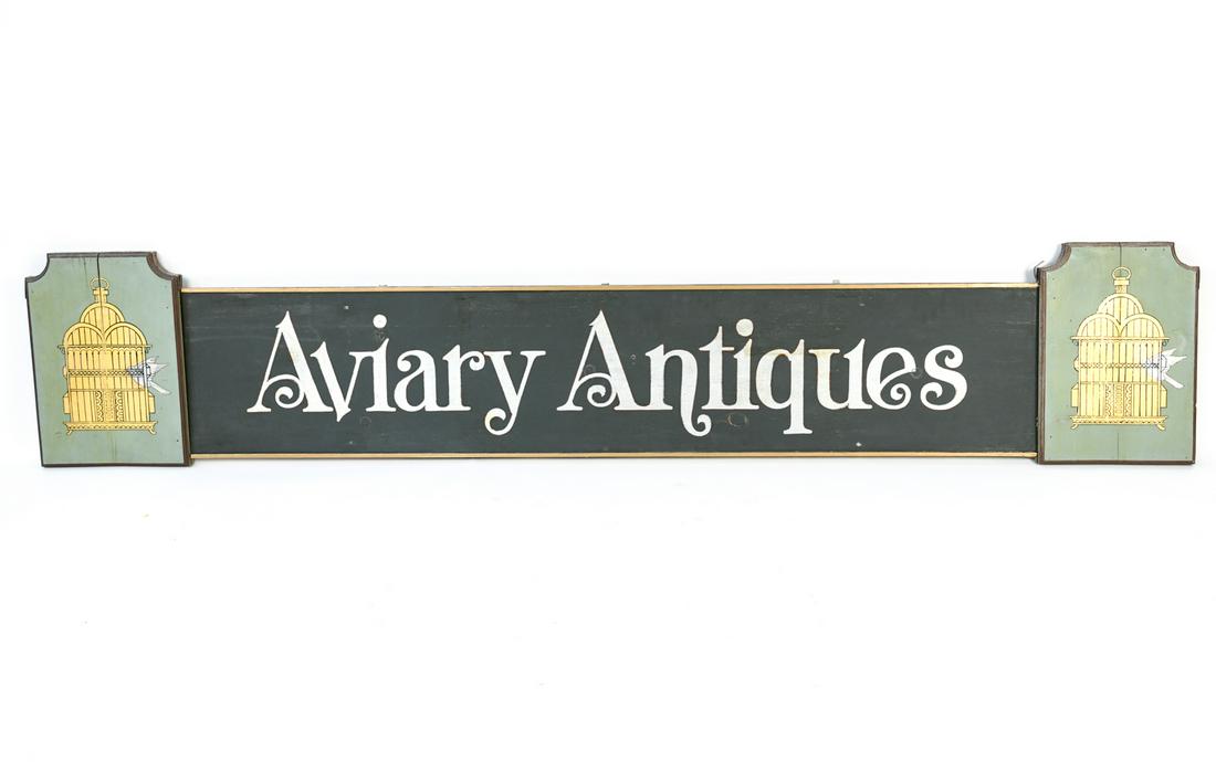 PAINTED WOODEN AVIARY ANTIQUES SIGN: Painted wooden sign with metal trim. Dimensions: H 15" x W 98" x D 3" Condition: Some metal trim lifting up. Paint loss. Few stress cracks to wood. Some nicks and marks. Few old repairs and areas of r