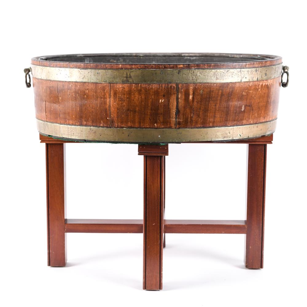 WINE BARREL BOTTLE COOLER ON STAND: Wooden wine cooler with metal insert. Brass trim and handles. Dimensions: H 24.5" x W 27" x D 19" Condition: Loss of finish to wood. Scratches and nicks throughout. Separation to joints.