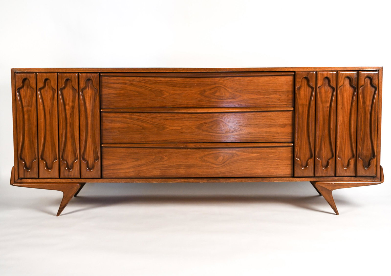 MID-CENTURY CREDENZA, MANNER OF VLADIMIR KAGAN: Mid-Century Modern credenza with Z-shaped legs and sculptural door fronts in the manner of Vladimir Kagan. Labeled Detroit Furniture Co. inside drawer. Dimensions: H 31" x W 76" x D 20" Condition: Wea