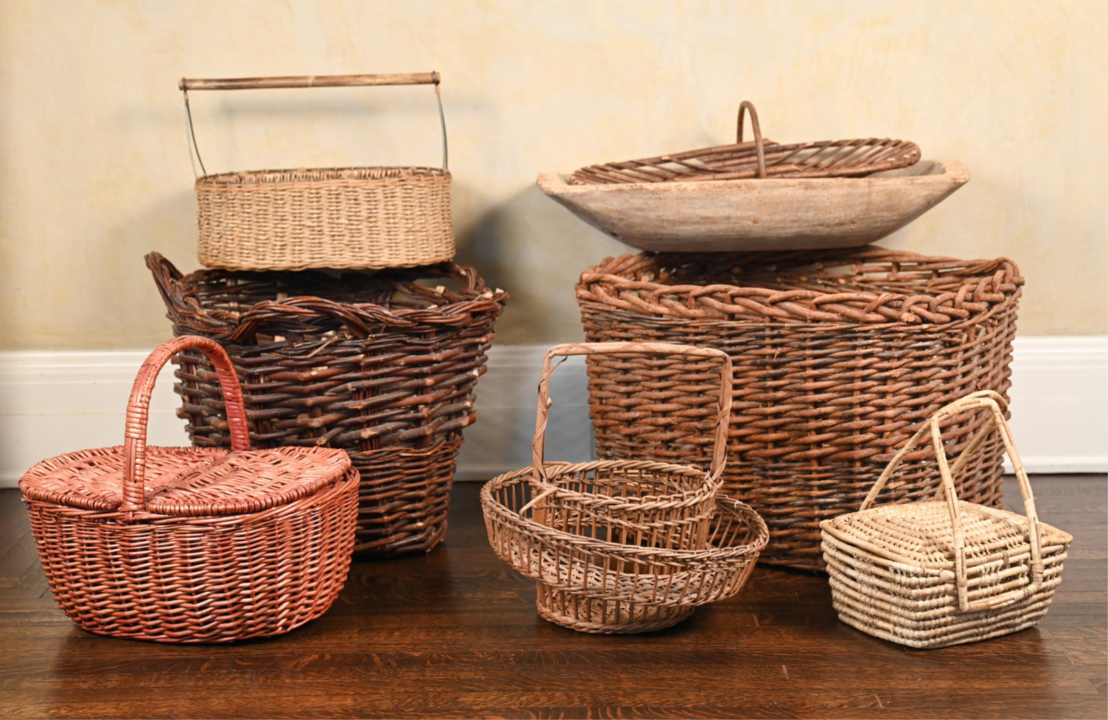 GROUPING OF WICKER BASKETS & WOODEN TRENCHER: (8) pieces. Dimensions: (Largest) H 18.5" x W 25" x D 22" Condition: Some breaks to wicker. Wear throughout consistent with age and use. Trough with worming, splits, and losses.