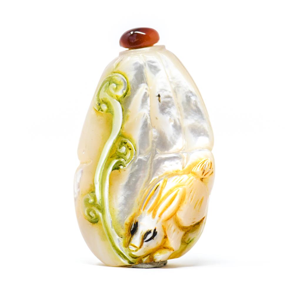 CHINESE CARVED MOTHER OF PEARL SNUFF BOTTLE: Chinese carved mother of peal snuff bottle with rabbit. Carnelian stopper with spoon. Dimensions: H 2.75" x W 1.75" x D .75" Condition: Repair to back, a few inclusions. Substance adhered to base to h