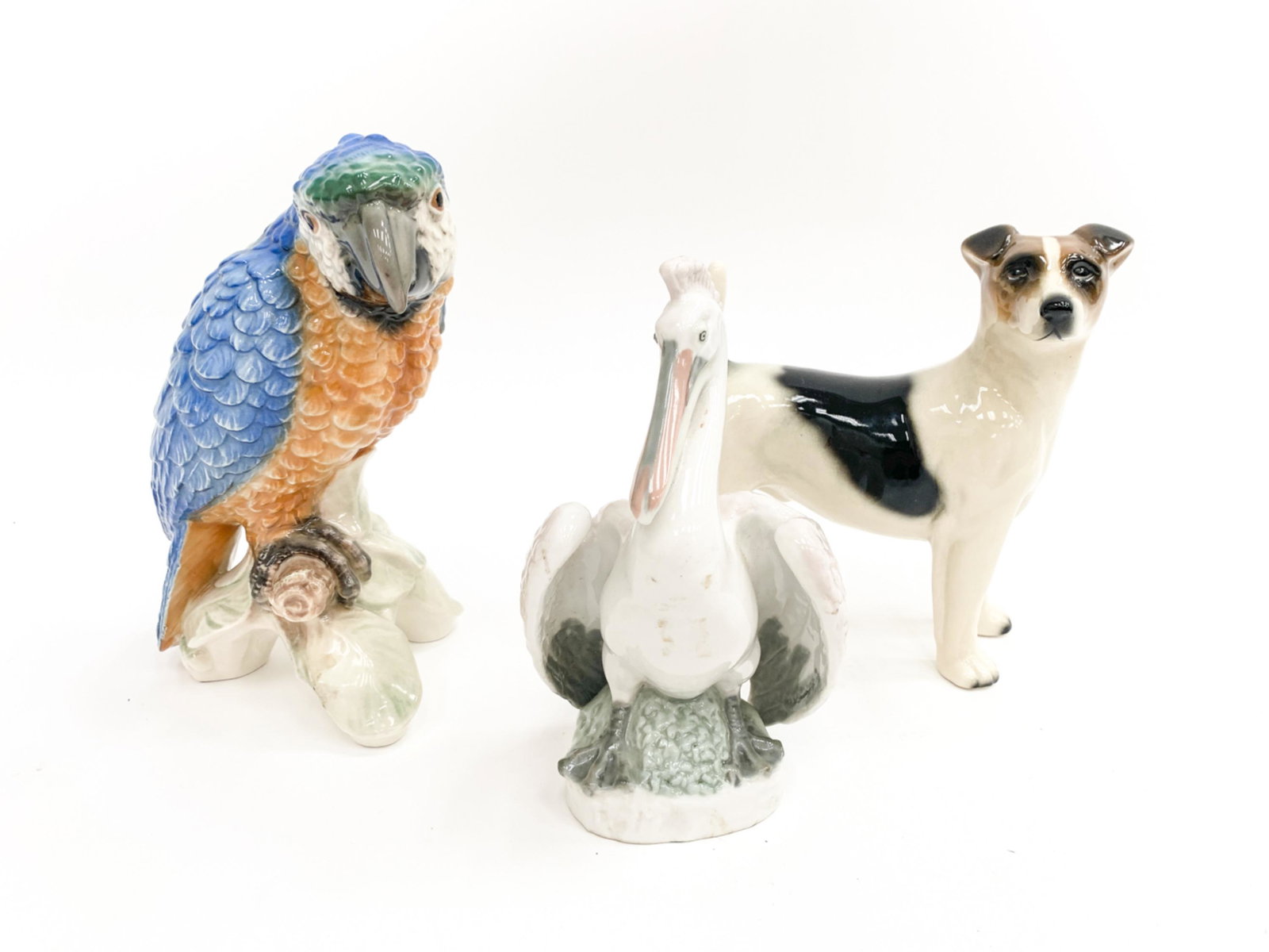 (3) PORCELAIN ANIMAL FIGURINES: Including Goebels parrot, German stork, and an English dog. Dimensions: (Parrot) H 9" x W 5" x D 7" Condition: No apparent damages.