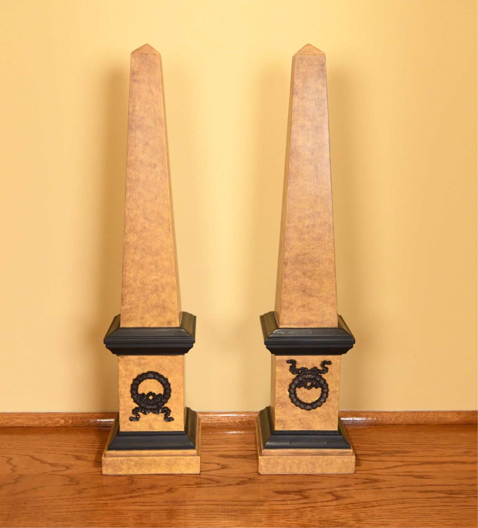 PAIR OF FAUX MARBLE OBELISKS: Faux painted wooden obelisks with applied ormolu wreaths. Dimensions: H 24" x D 5.5“ Condition: One with loose wreath in front. Minor craquelure to some areas of the paint finish.