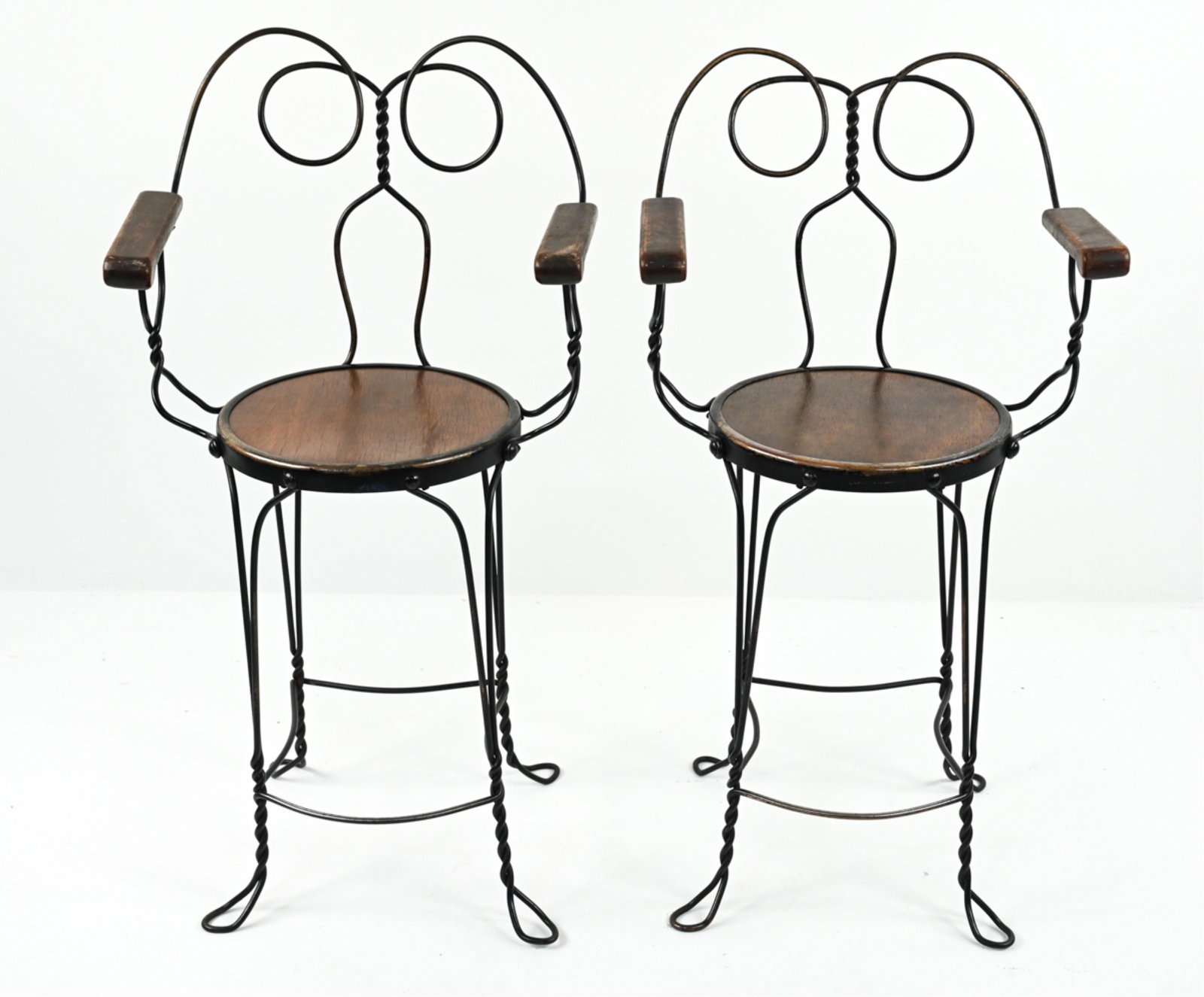 PAIR 20TH C. ICE CREAM PARLOR HIGH-TOP ARMCHAIRS: Unique pair of vintage ice cream parlor-style bar or counter armchairs in twisted wrought iron and wood. Dimensions: H 40" x W 22" x D 18", SH 25" Condition: Wooden seating surface appears to have bee