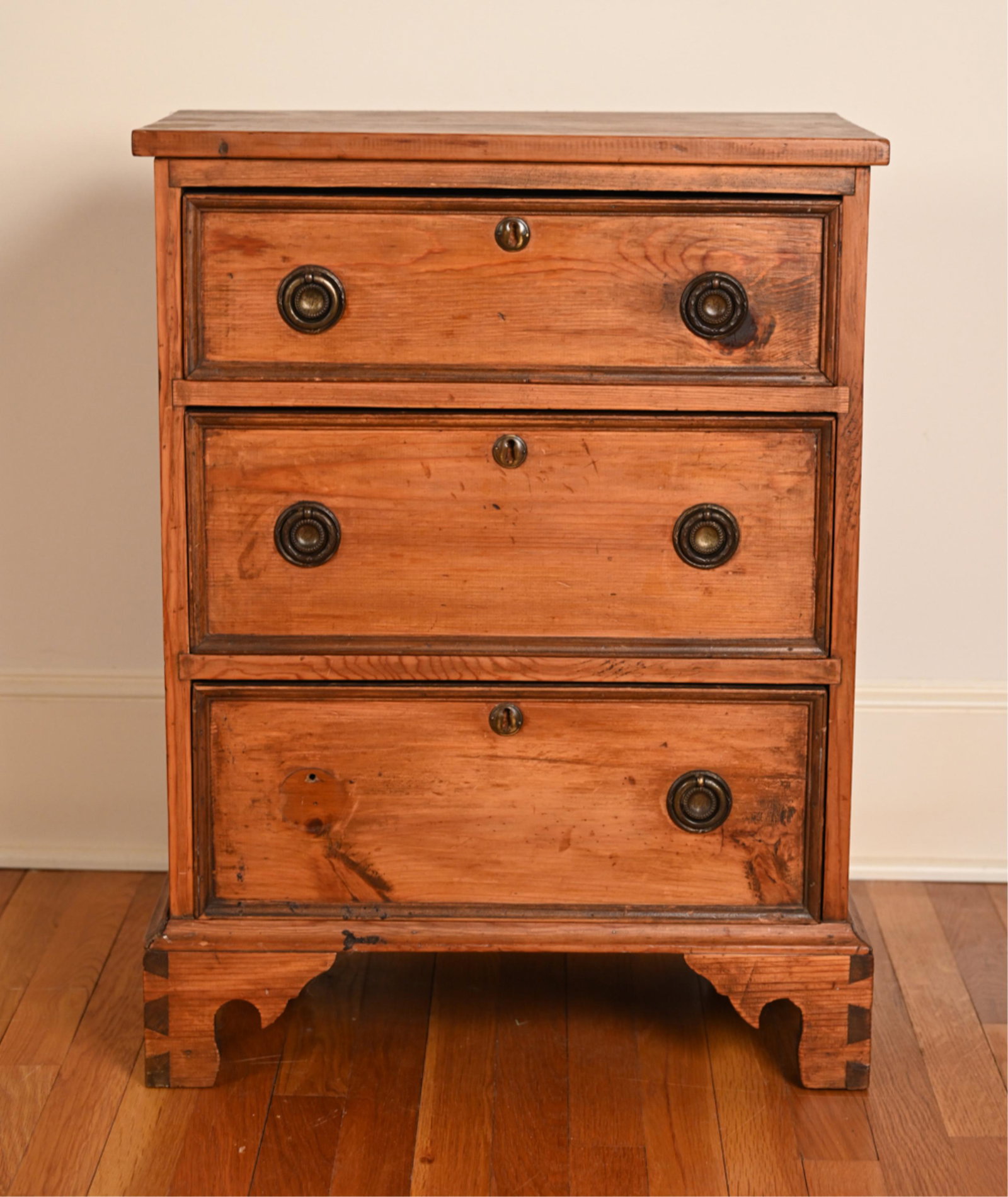 VINTAGE THREE-DRAWER CHEST/NIGHTSTAND: Bracket feet. Diminutive chest as end table or nightstand. Dimensions: H 29" x W 22.25" x D 13" Condition: Missing one handle to bottom drawer. Wear throughout including losses to wood, scratches, scu
