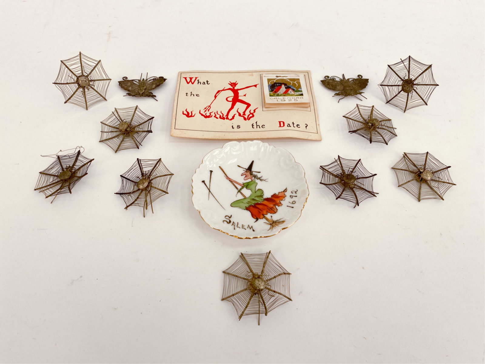 ANTIQUE HALLOWEEN/MACABRE GROUPING: Including a Salem witch painted Limoges saucer, a 1925 calendar, and a grouping of metal spider webs with spiders. Dimensions: (Calendar) H 6" x W 4.25" Condition: Some bends and losses in the metal.