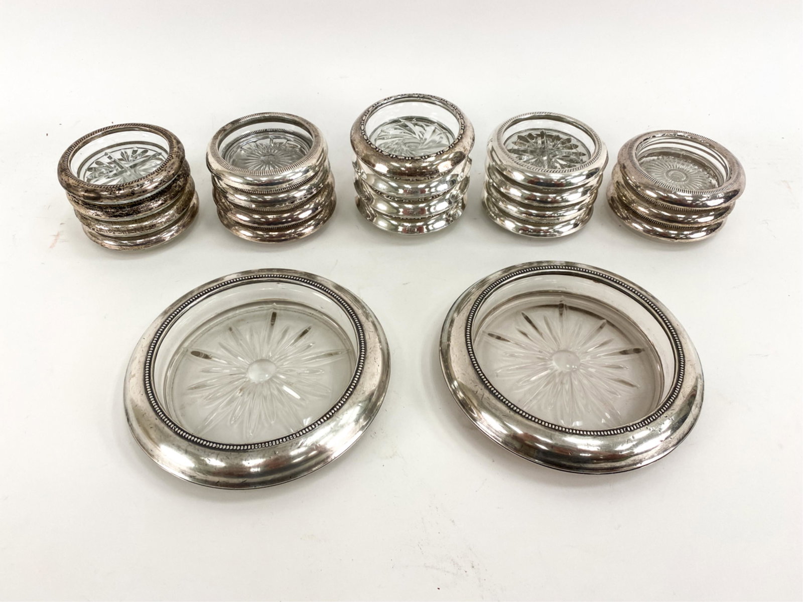 (21) STERLING COLLARED GLASS COASTERS: Including (2) wine bottle size and (19) glass size. Different manufacturers and designs. All marked sterling. Dimensions: (Largest) Dia. 7" Condition: Used, silver with some dents and tarnish.
