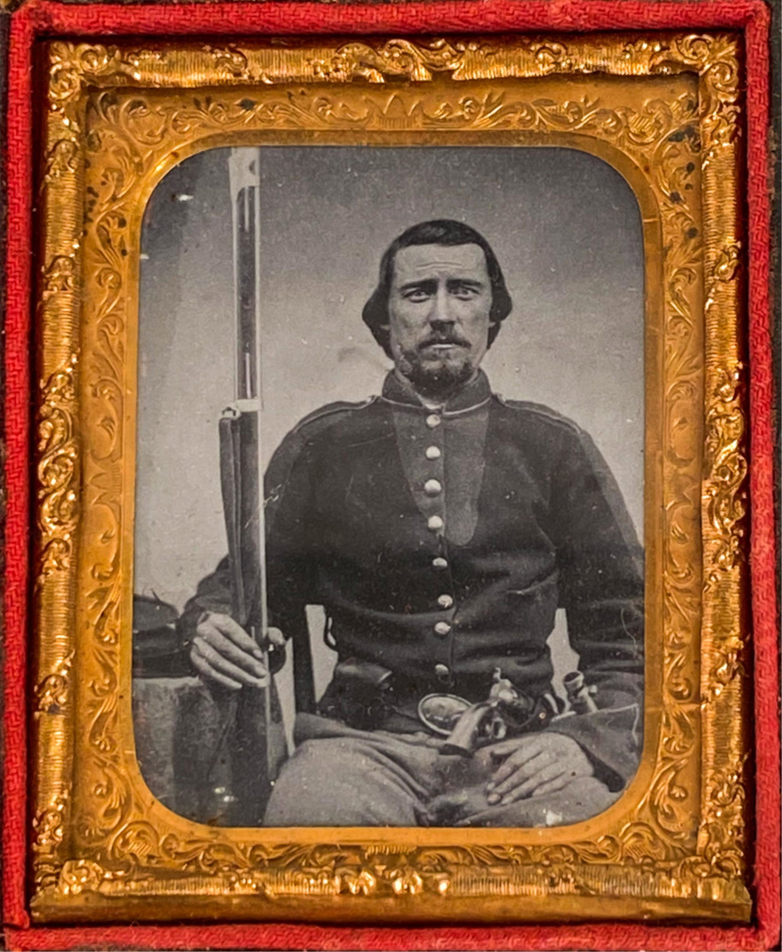 1/9 PLATE CIVIL WAR SOLDIER AMBROTYPE: Soldier in irregular outfit, seated holding rifle. Pistol in his belt. Dimensions: (Case) H 2.75" x W 2.25" Condition: Cover broken off case. Interior photograph appears good and clean. Some wear to t
