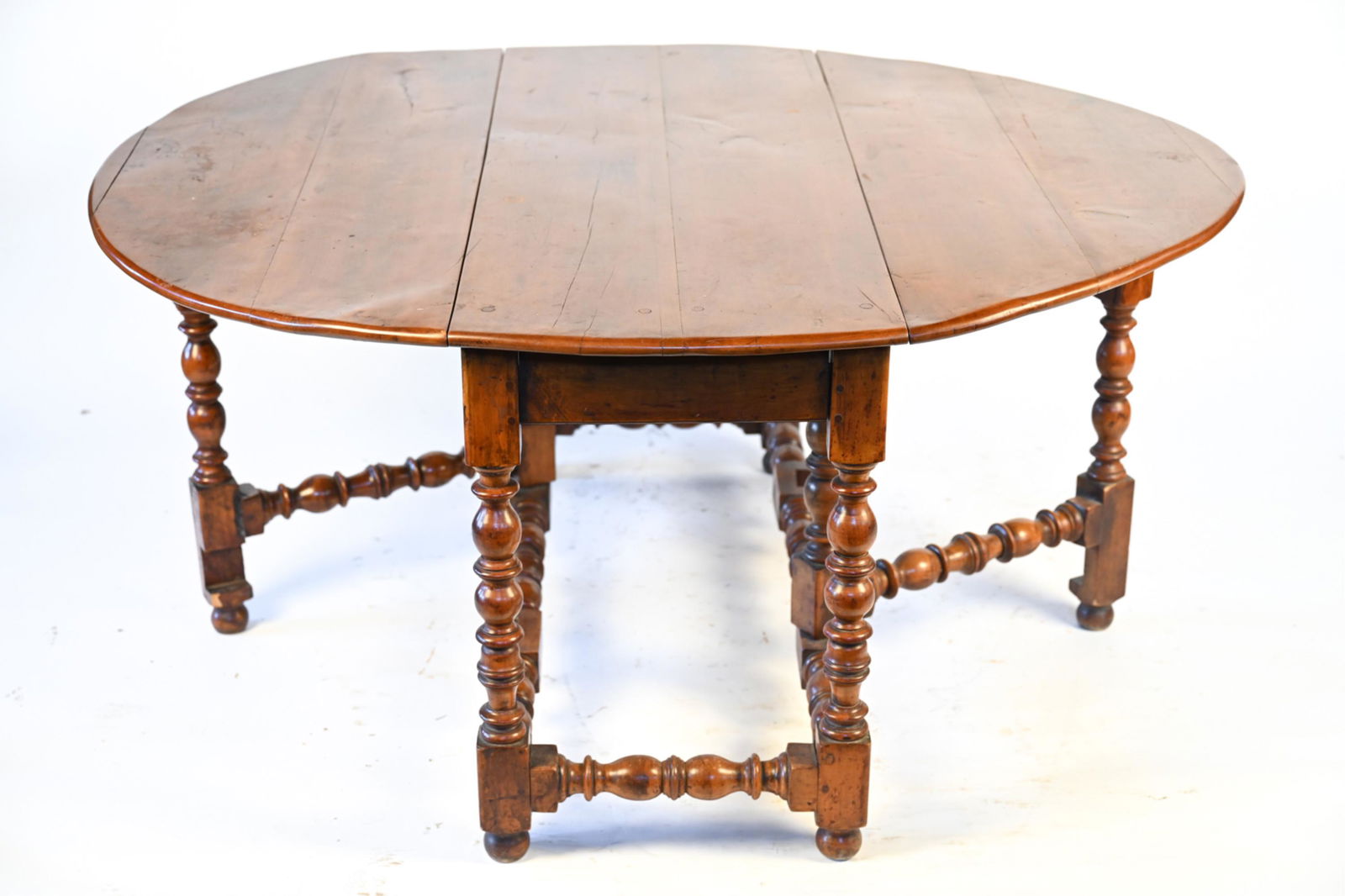 ANTIQUE GATELEG DINING TABLE: Dining table with two large drop leaves, supported by four stationary legs and two gatelegs connected with stretchers, each fully turned with vase-and-ring motifs. Solid wood with rich antique patina