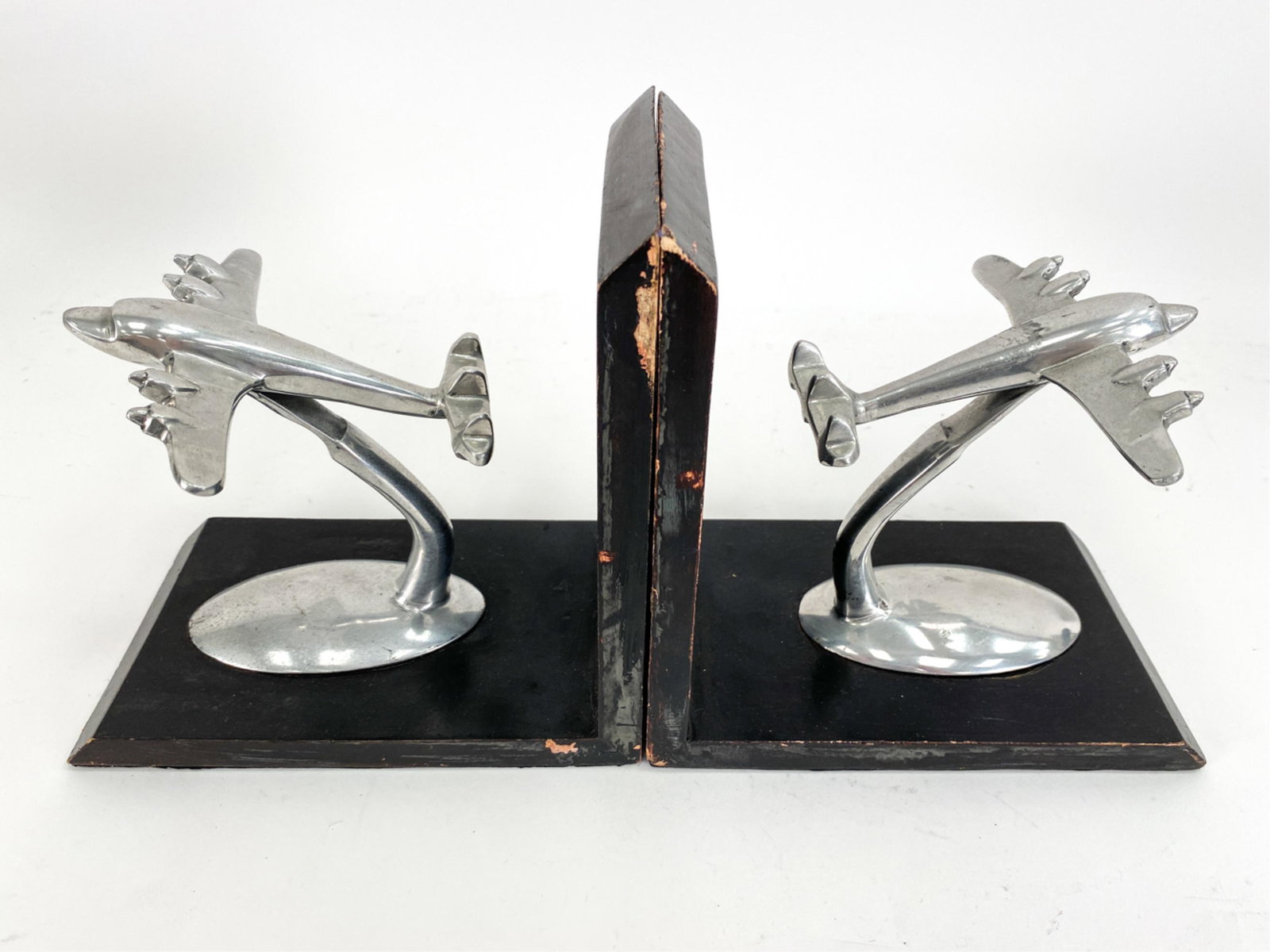 PAIR OF DECO STYLE AIRPLANE BOOKENDS: Planes in cast metal on black painted wood. Unmarked. Dimensions: H 8" x W 8" x D 4.75" Condition: Rubbing, losses to paint, some surface damage to metal.