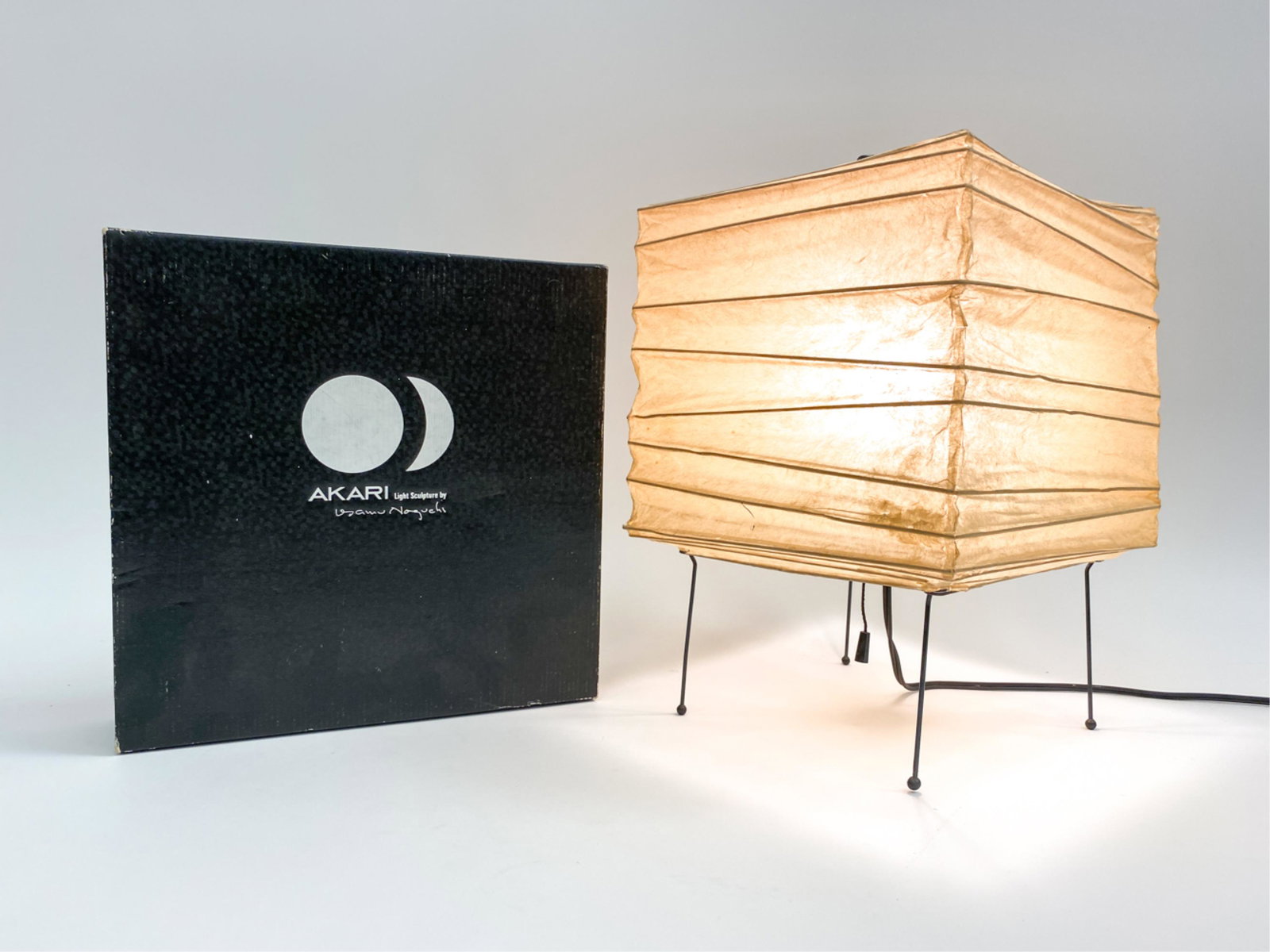 EARLY ISAMU NOGUCHI AKARI 3X PAPER SHADE LAMP: Early example of Isamu Noguchi Akari light sculpture from the 3 X series. With original box. Marked with small sun and moon to bottom of shade. Dimensions: H 13.25" x W 9.25" x D 9.5" Condition: Few s