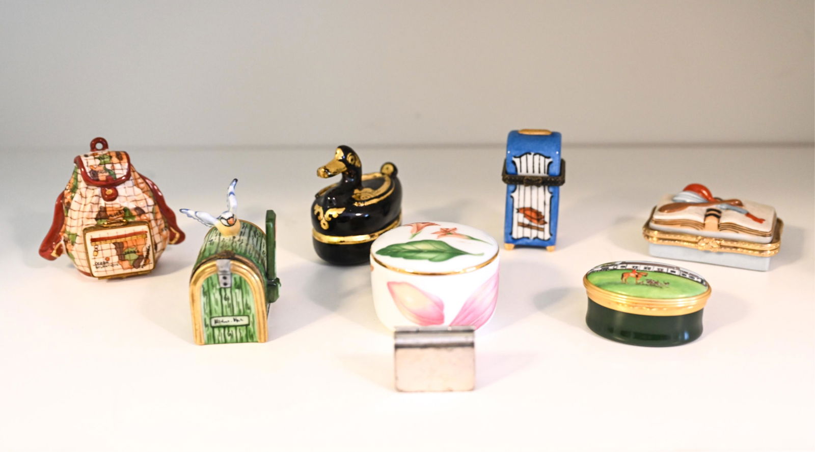 GROUPING OF TRINKET / PILL BOXES: Including Mexican sterling box, Halcyon Days enamel hunt club box, Tiffany & Co. Tiffany Flowers porcelain box, lacquer duck box, Rochard Limoges hand-painted backpack box, Parasol Collections Limoges