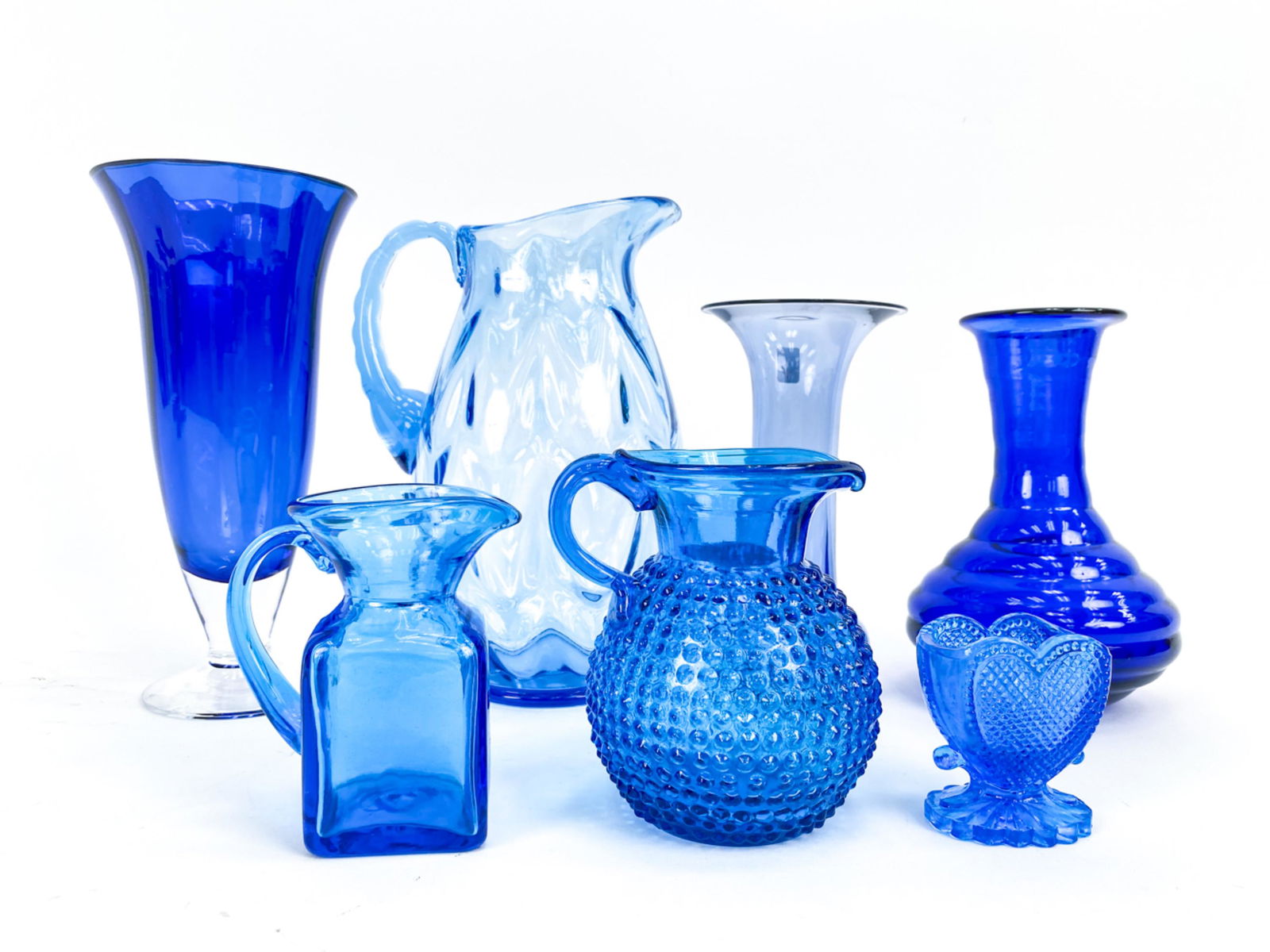 (7) BLUE ART GLASS VESSELS: Including a Fostoria pitcher, vase marked Illum Holmegaard, etc. Dimensions: (Tallest) H 9.5" Condition: Few minor surface marks.