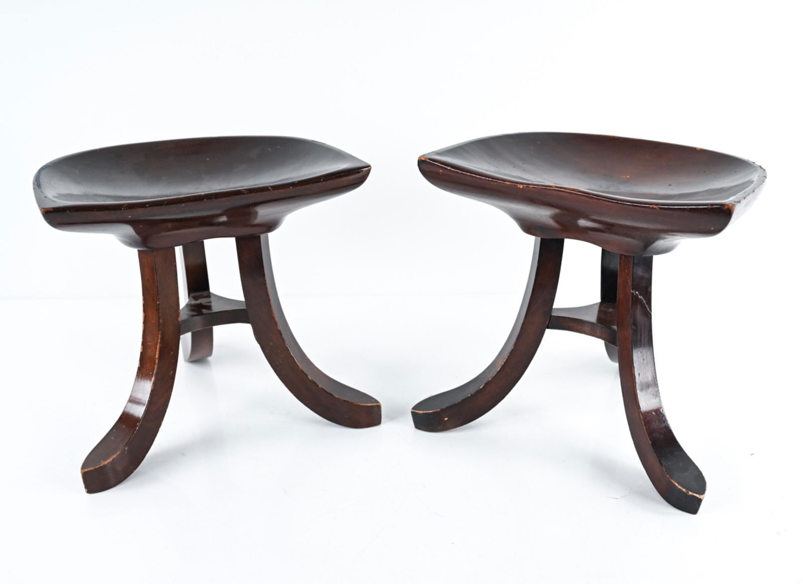 (2) EGYPTIAN REVIVAL STOOLS, MANNER OF ADOLF LOOS: Pair of petite stools in sculpted mahogany, in the manner of the "Theban" stool by Adolf Loos. Dimensions: H 13.5" x W 14.5" x D 11.5" Condition: One stool with repaired breaks to two legs, the other