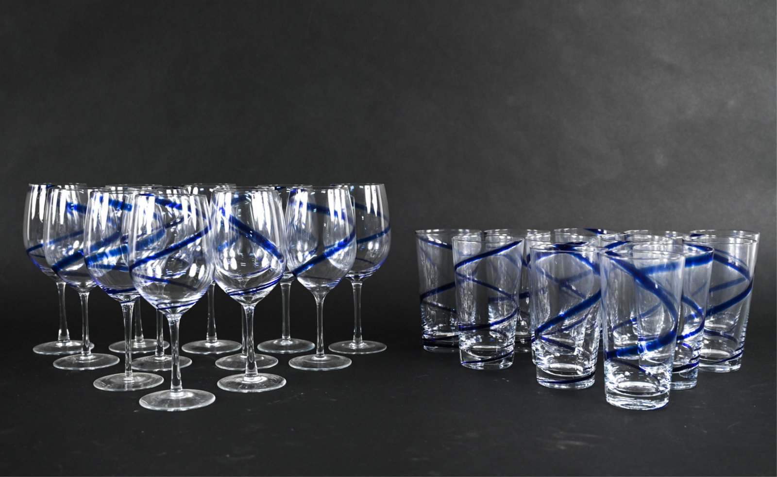 GROUPING OF ART GLASS COBALT SWIRL BARWARE: Including (12) wine goblets and (12) highball tumblers. Apparently unsigned. Dimensions: (Wine) H 9" x Dia. 3.5" Condition: No issues to note.