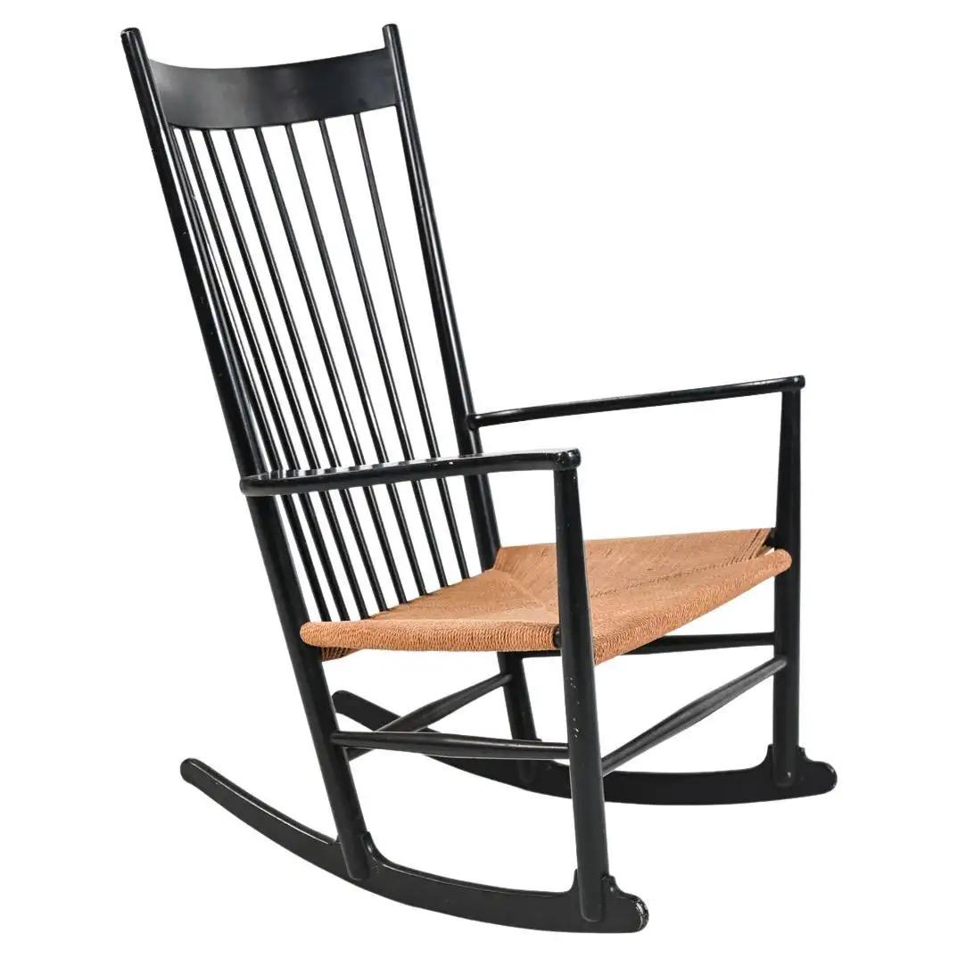 HANS J. WEGNER FOR FBD MOBLER J-16 ROCKING CHAIR: The iconic J-16 rocking chair by Hans Wegner represents a Danish update on a classic Windsor silhouette, with elongated delicate turned spindles, braided papercord seat, and matte black lacquered fini