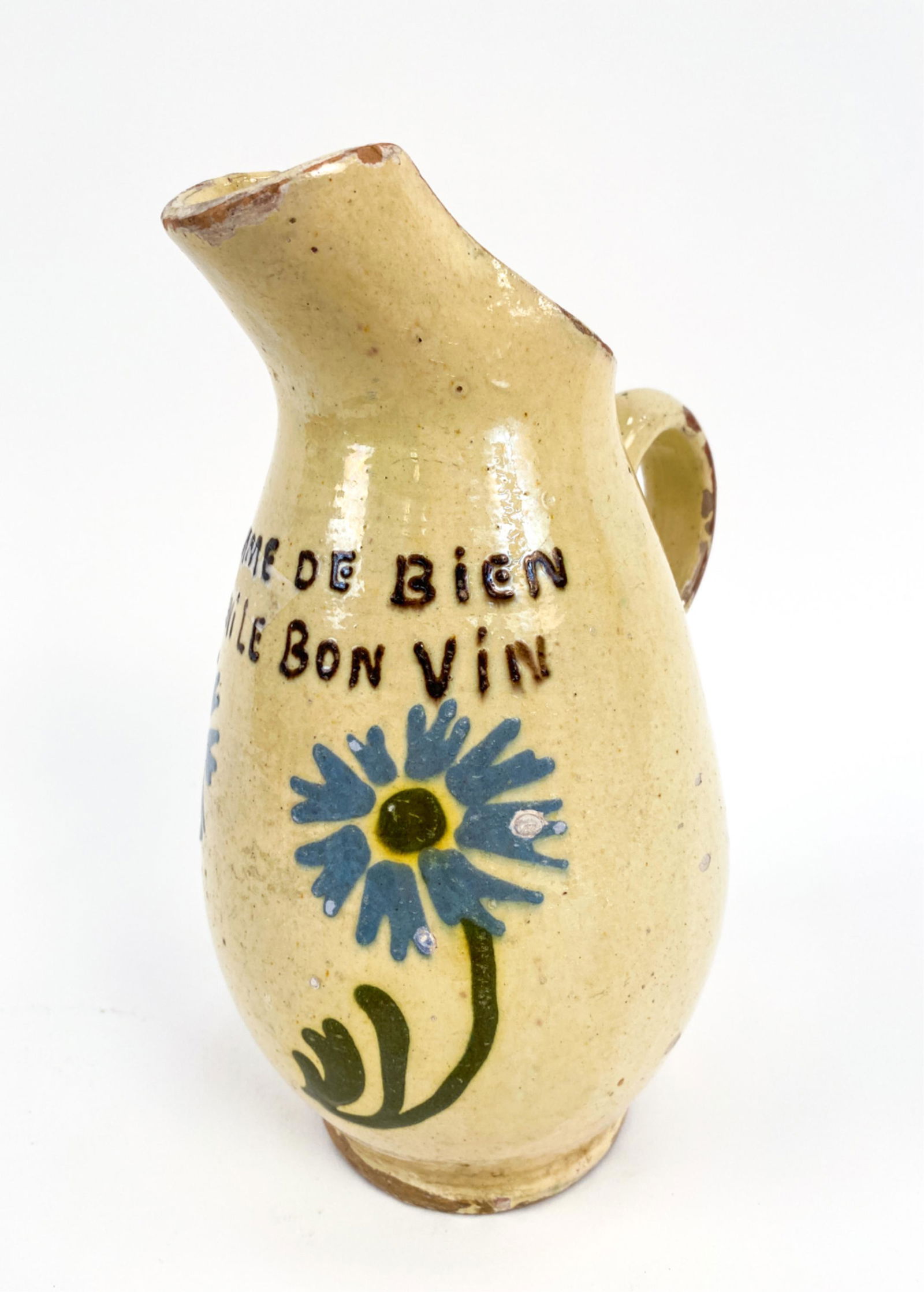 20TH C. FRENCH ANTIQUE "TALKING SAVOIE PITCHER": With a humorous idiom. Alpen flowers. "A good man never dislikes good wine" cider pitcher. Dimensions: H 9" x W 6" x D 4.75" Condition: Old chips and glaze losses. Small firing cracks at handle termin